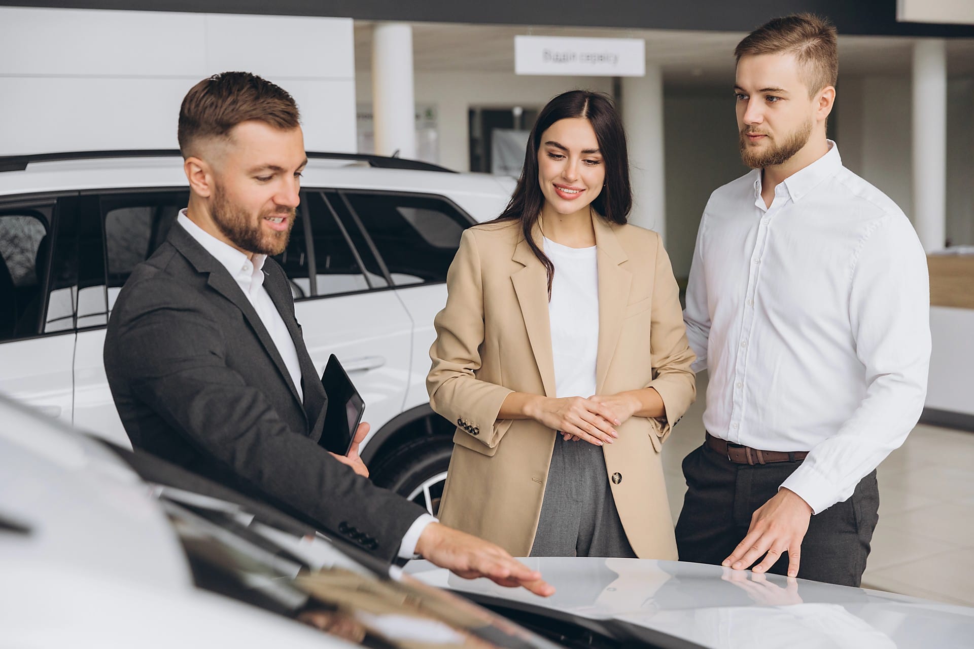 Aeroguard 360 PRO & Premium A car salesperson shows a couple features on a car inside a showroom. The man gestures towards the car's bonnet while the couple listens attentively. Other cars are visible in the background.