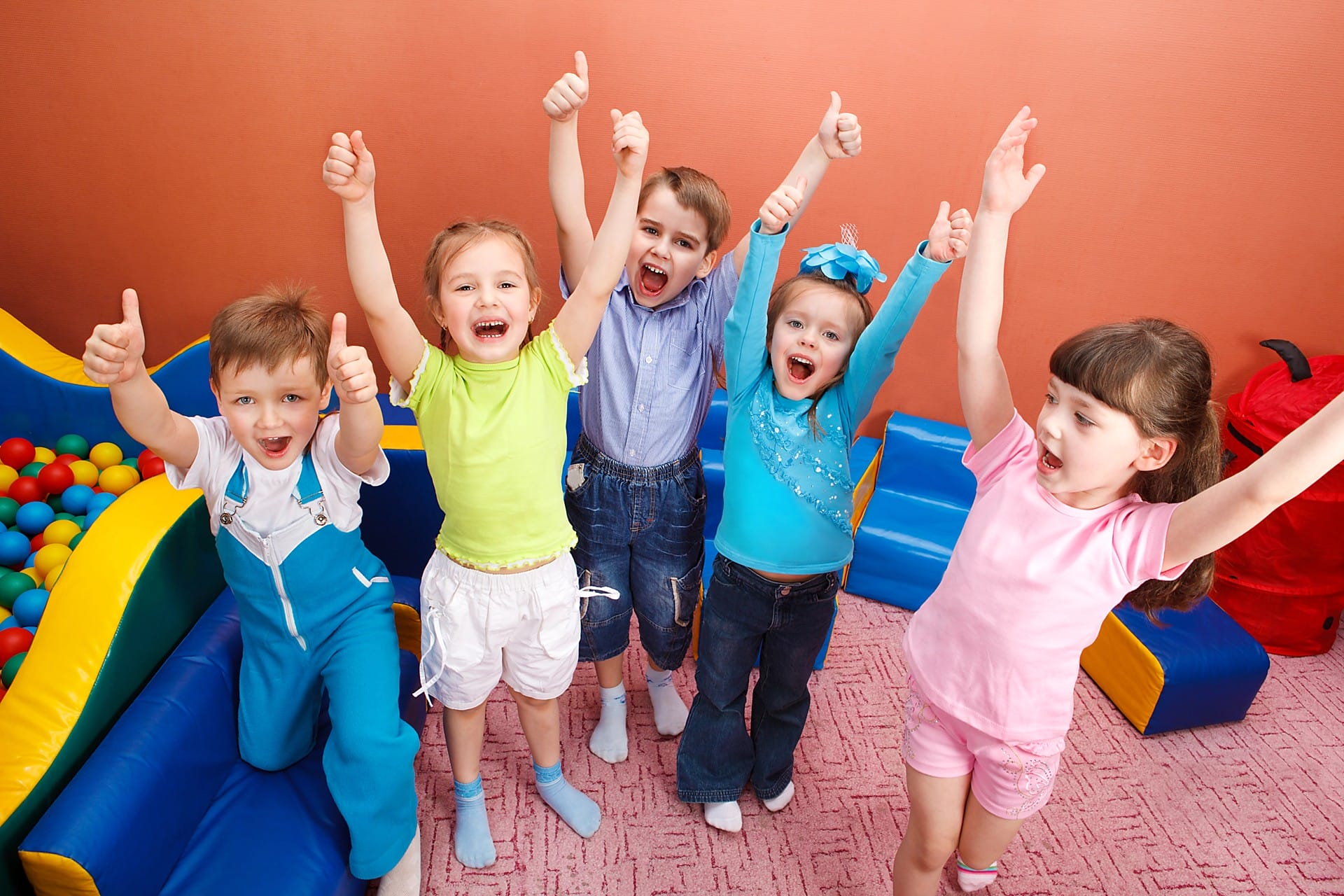 Aeroguard 360 PRO & Premium Five young children standing in a playroom with colourful toys, smiling and raising their arms with thumbs up, appearing happy and excited.